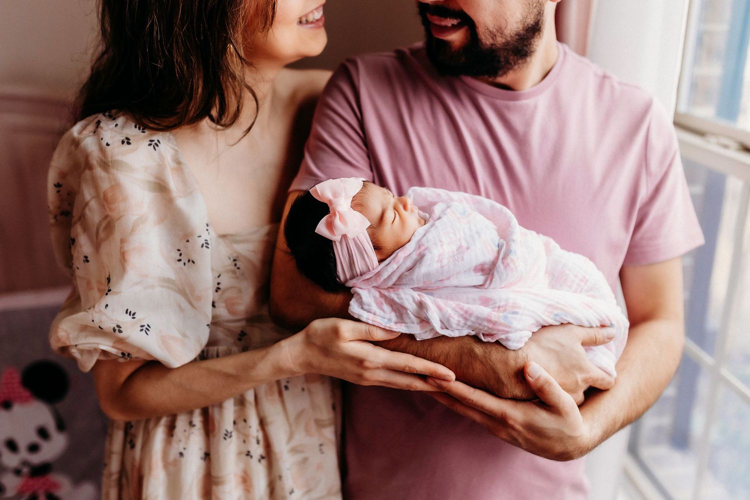 An intimate portrait of parents in soft lighting holding their newborn wrapped in white.