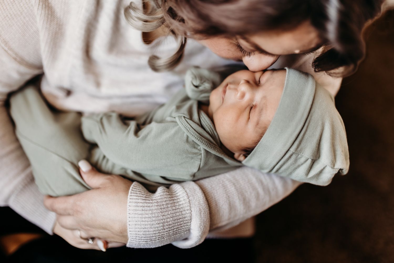 A newborn baby wrapped in sage green fabric being cradled tenderly.