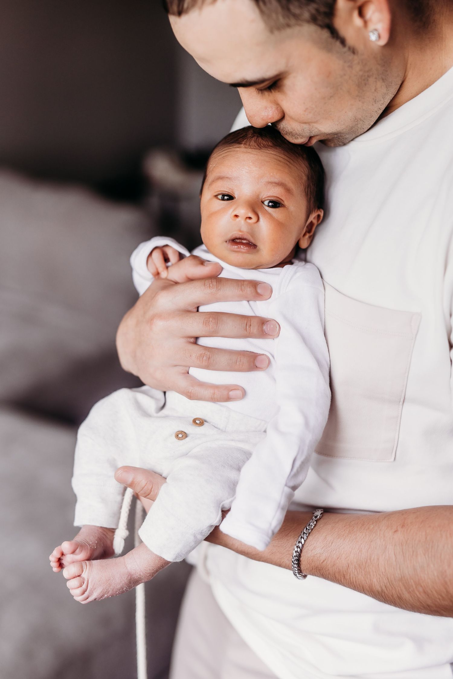 A parent in white holding a small baby wearing a white onesie.
