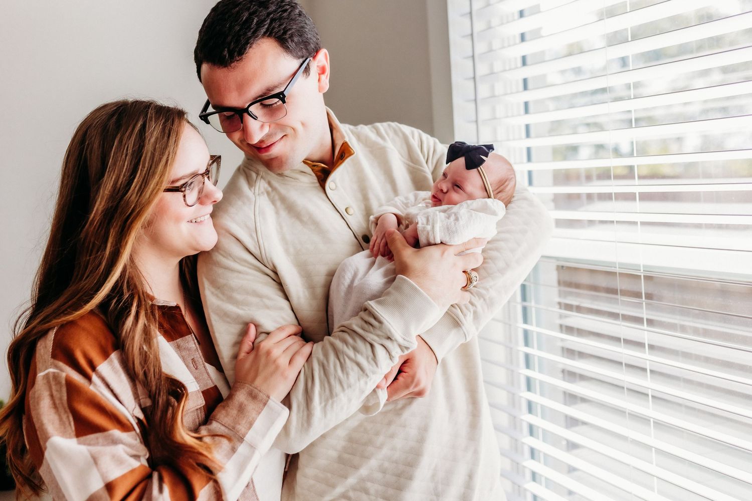 A tender family moment by window light with parents looking at their newborn.