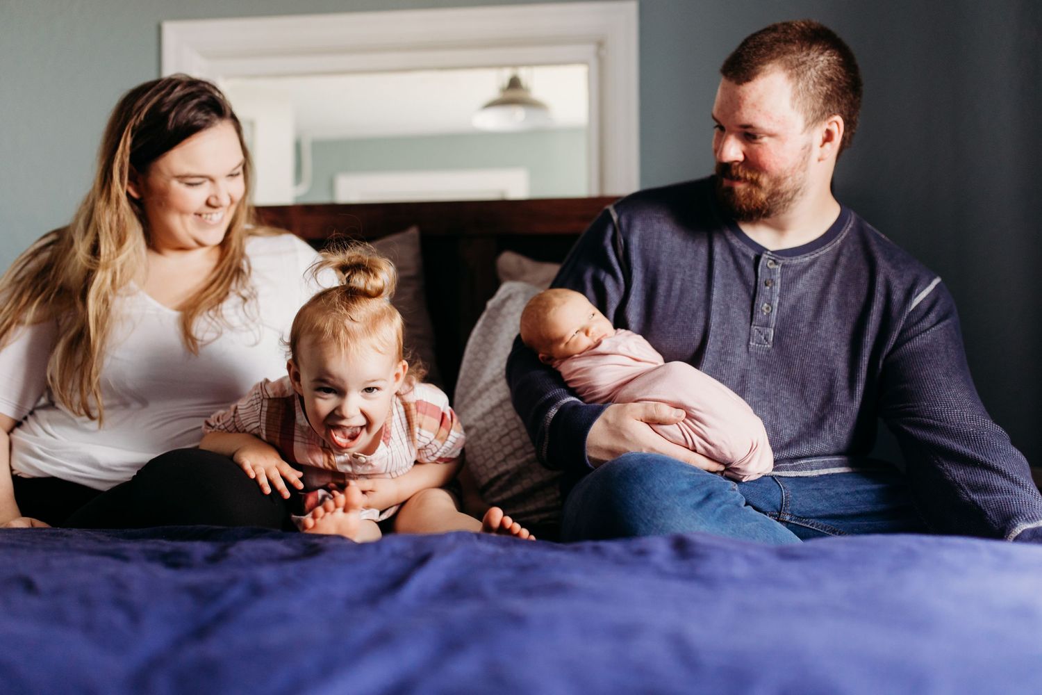 Family relaxing together on blue bed during casual lifestyle photo session.