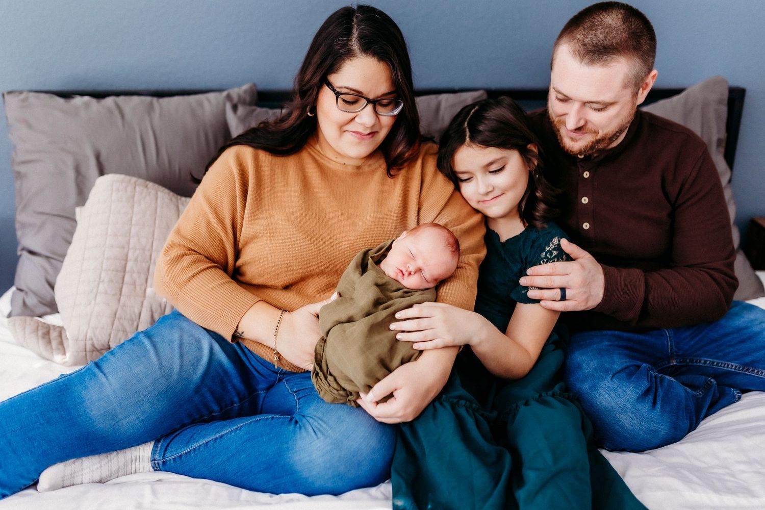A cozy family scene on a gray couch with everyone gathered around a baby.