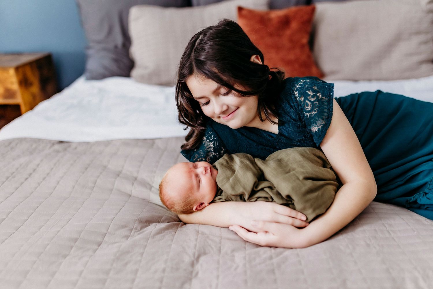 A tender moment between mother and baby resting together on a gray bed.