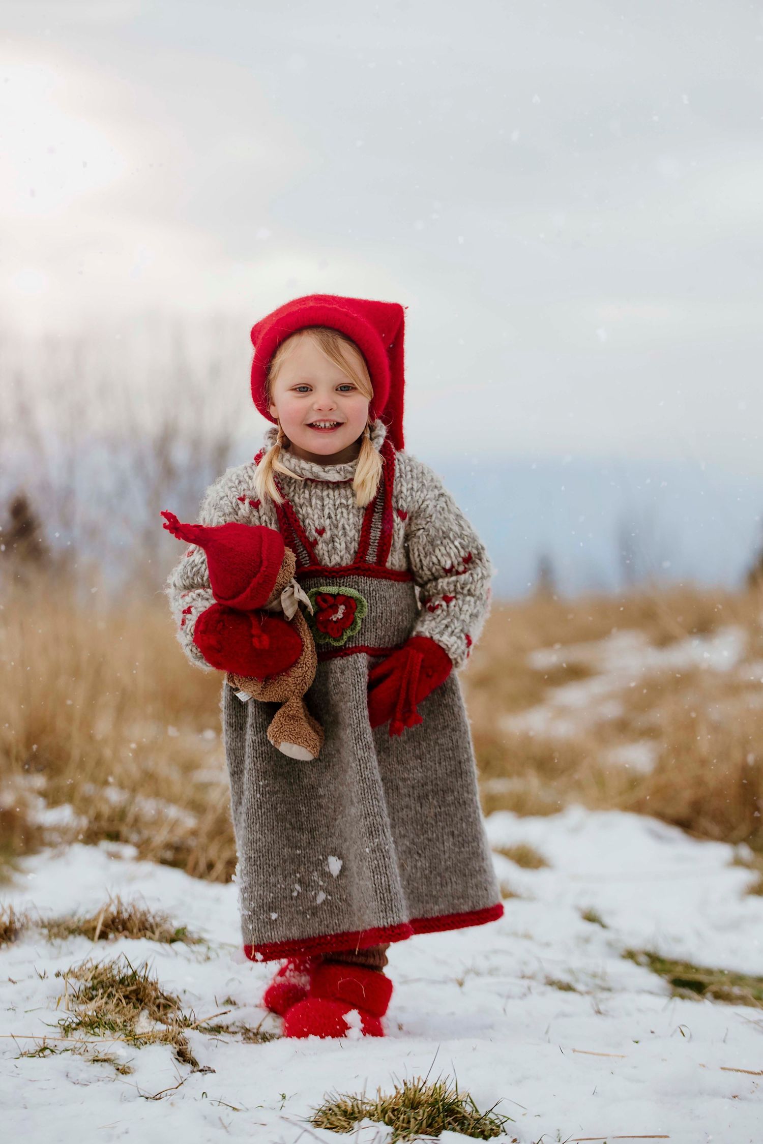 Small figure in red winter clothing and gray sweater playing in snowy field during winter.