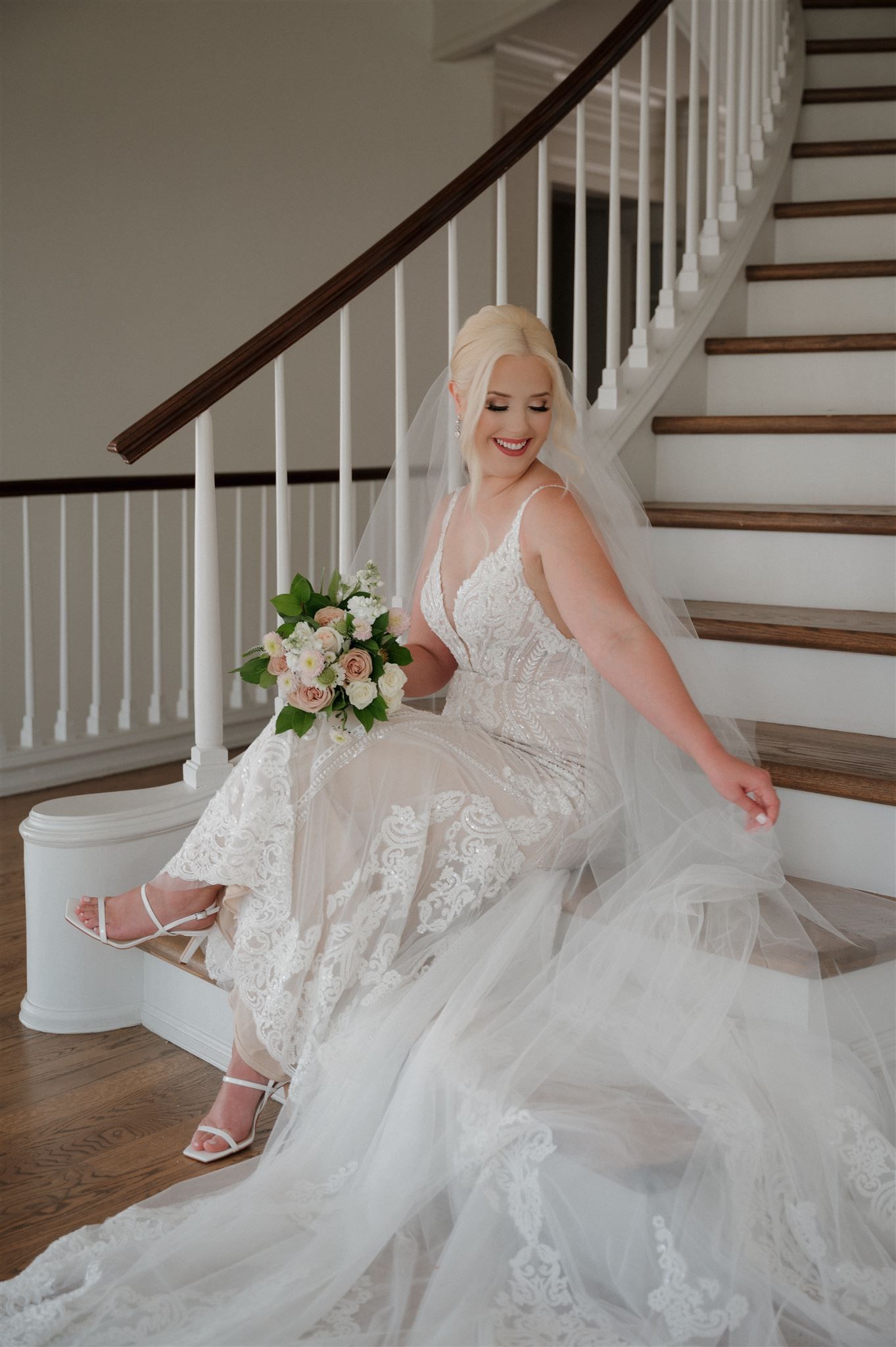 Joyful bridal portrait on staircase featuring flowing lace gown and elegant bouquet.