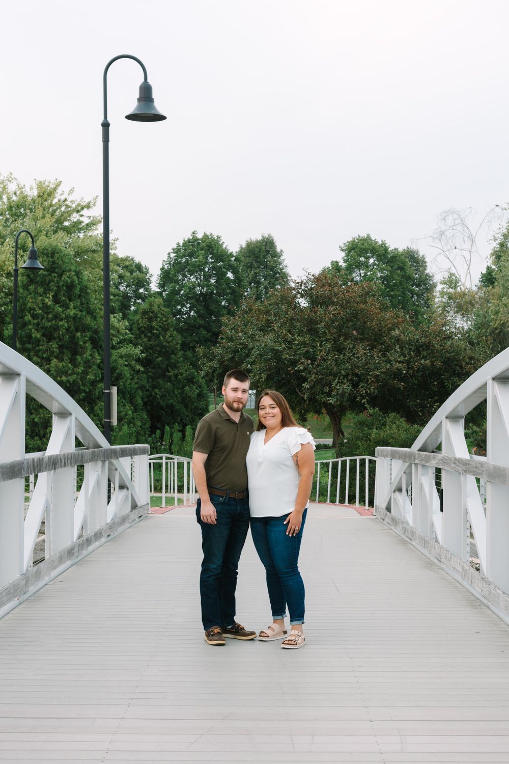 Happy couple standing together on a white bridge with a decorative lamp post.