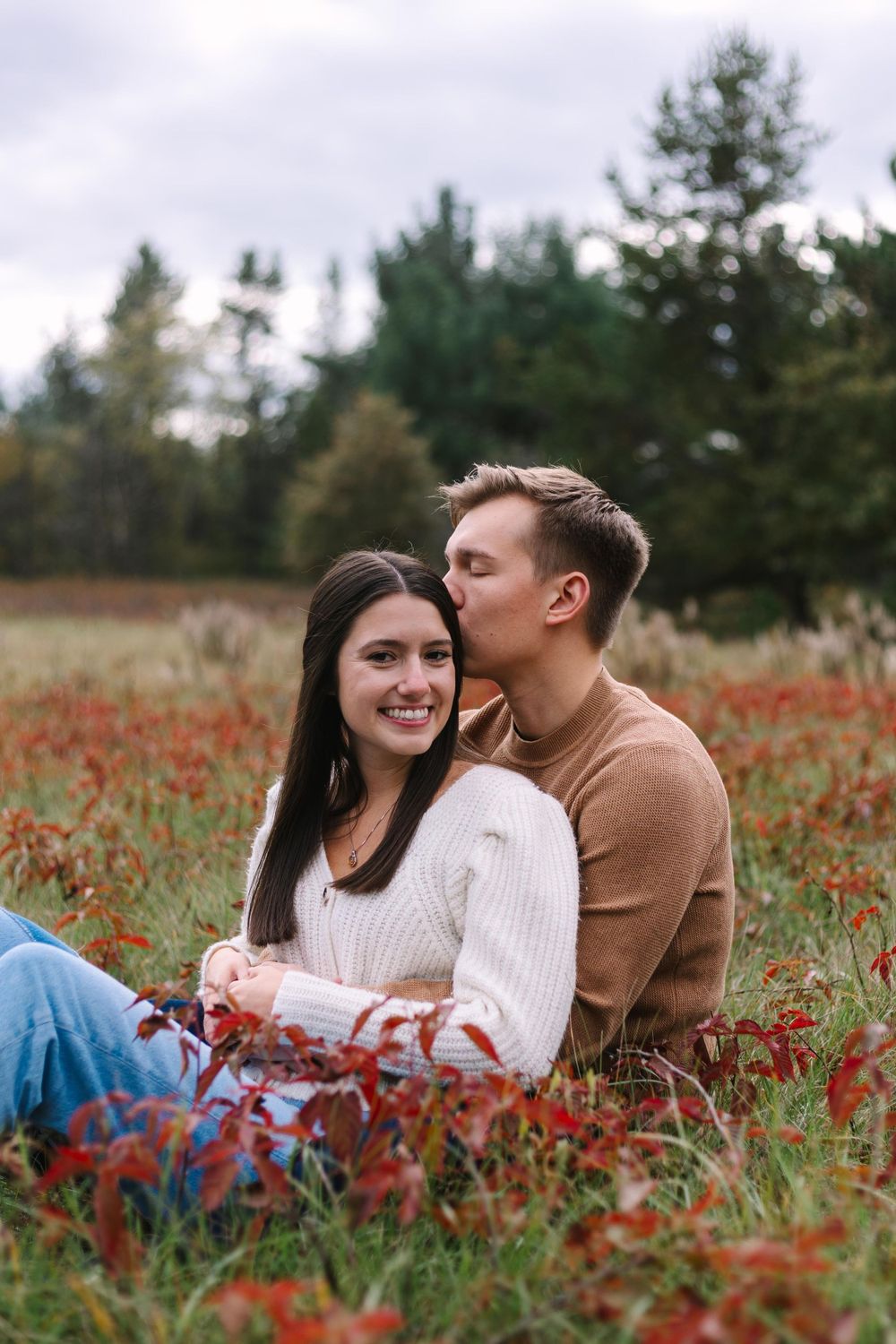 A couple sharing an intimate moment while sitting in a field of red autumn flowers.