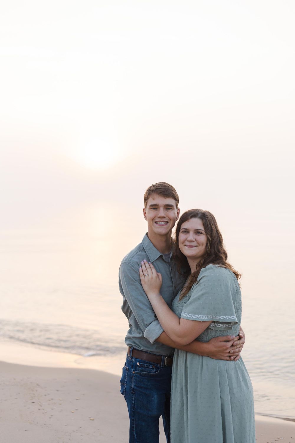 A couple embraces on a beach during sunset wearing coordinated casual outfits.