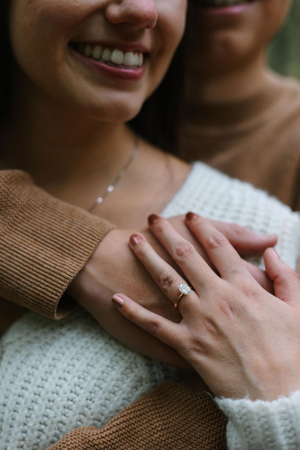 Close-up of hands showing an engagement ring with knit sweaters in the background.