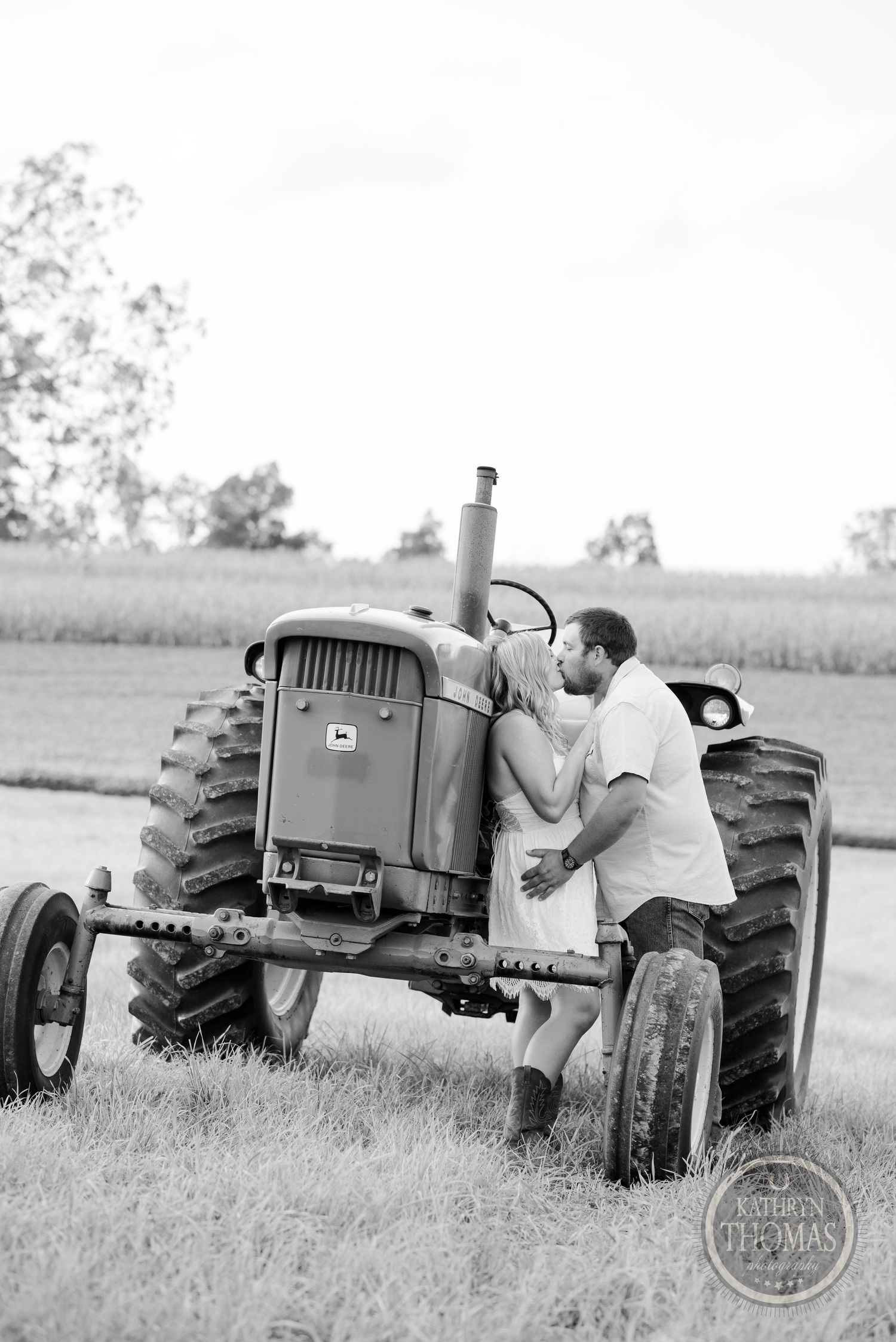 Black and white photo of couple sharing intimate moment on antique farm tractor.