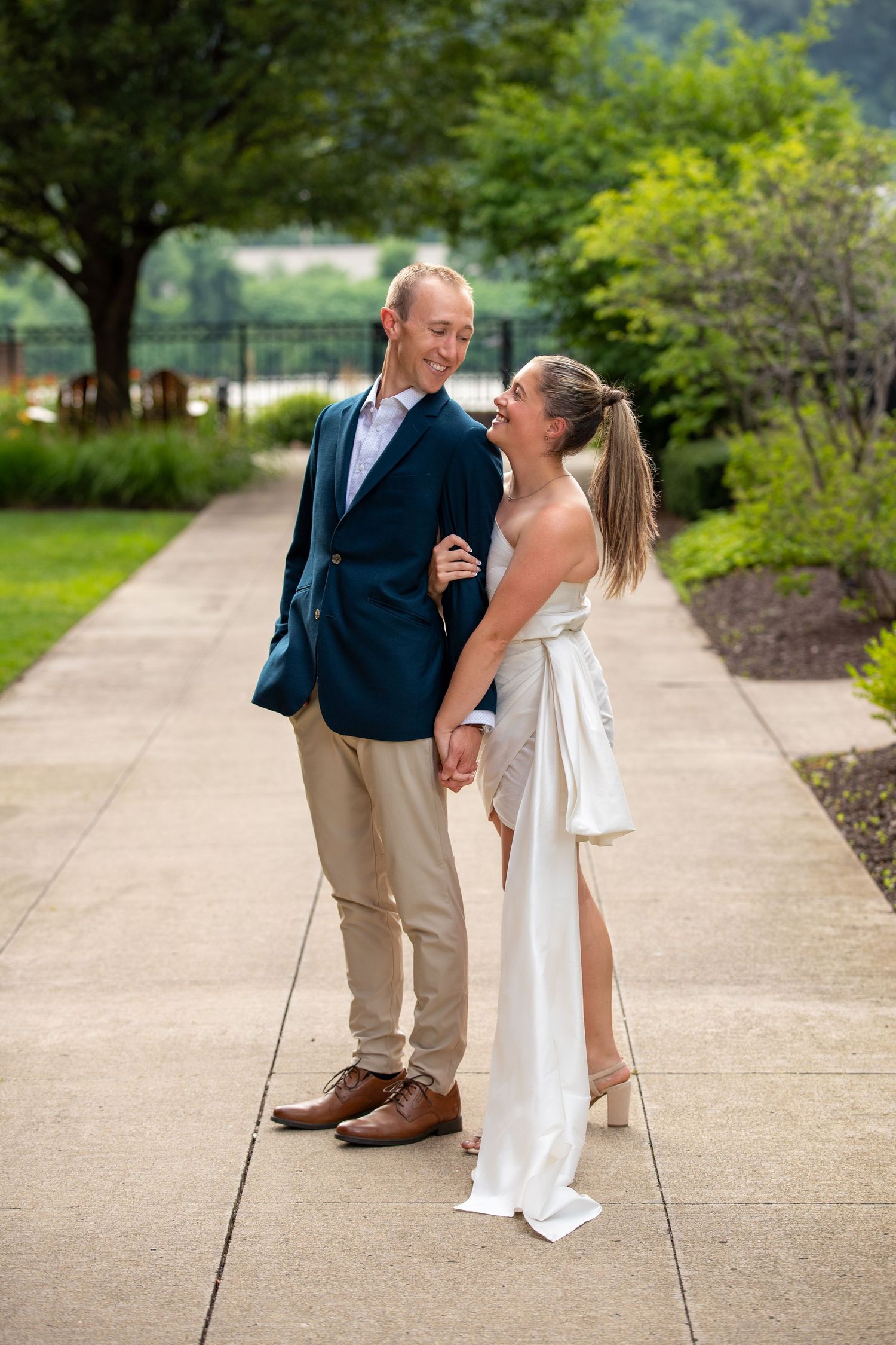 A couple shares a joyful moment together on a garden pathway during a summer wedding photoshoot.