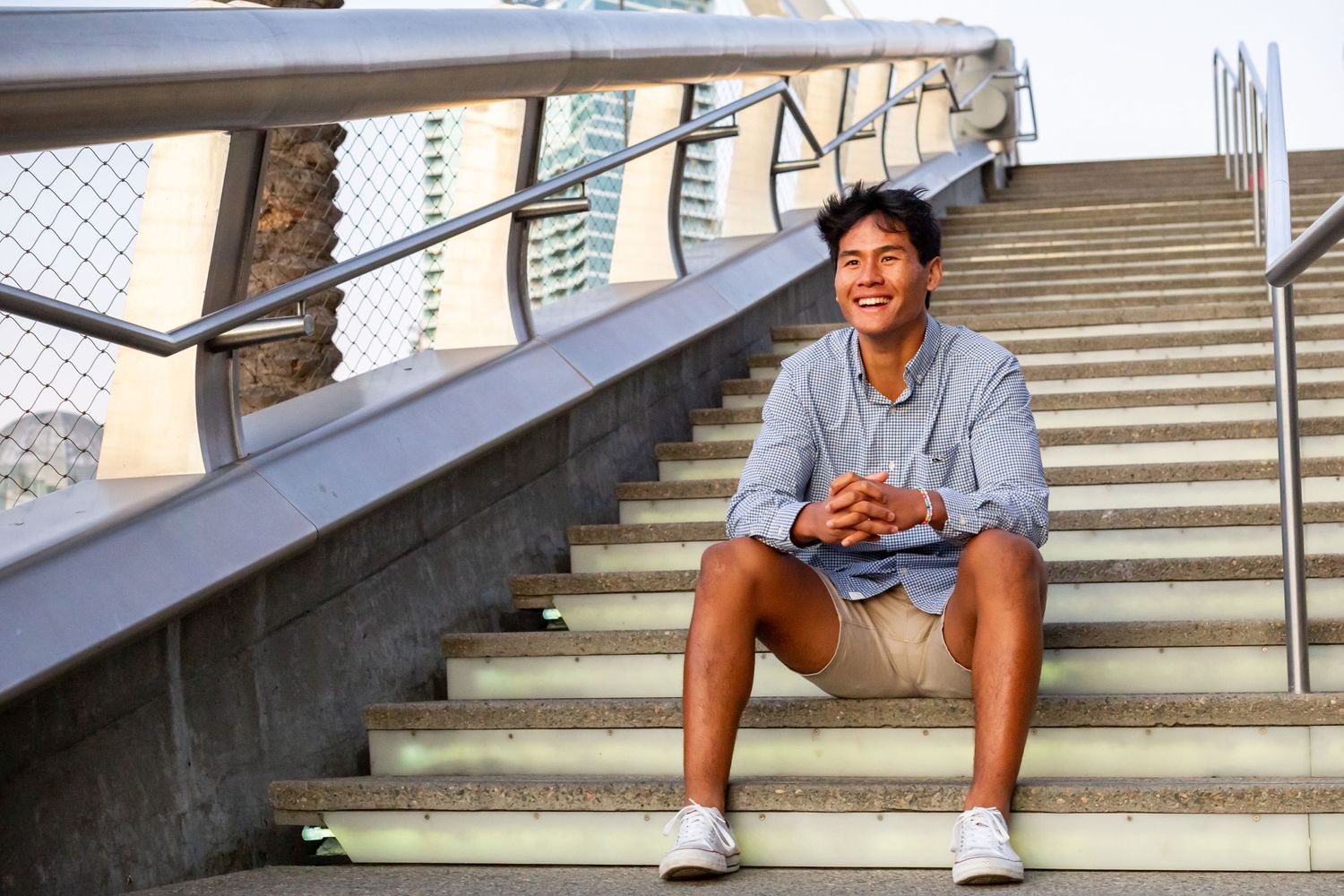A person sits casually on concrete steps outdoors wearing shorts and a gray t-shirt.