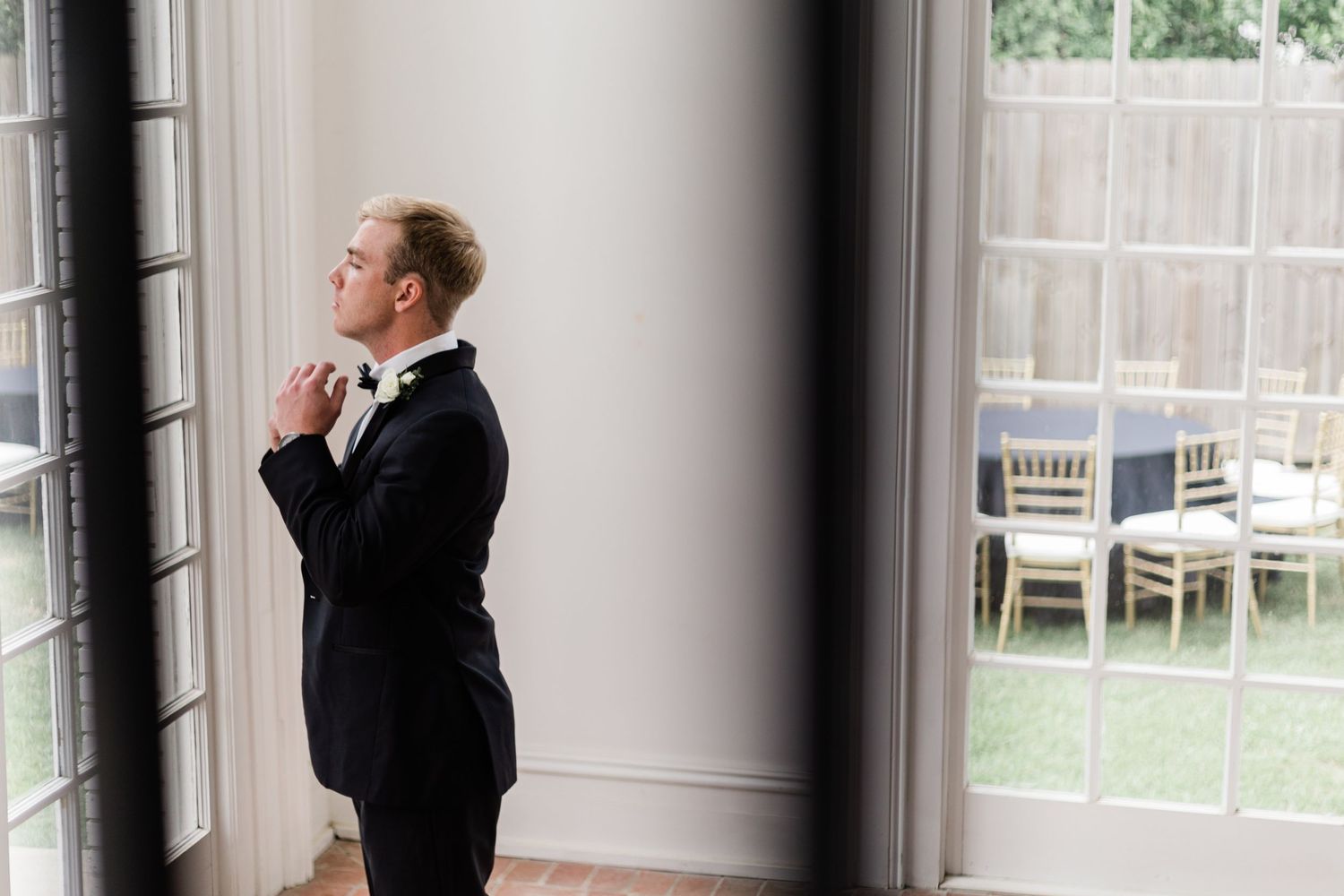 Artistic wedding day photo through window frame showing groom adjusting tie.
