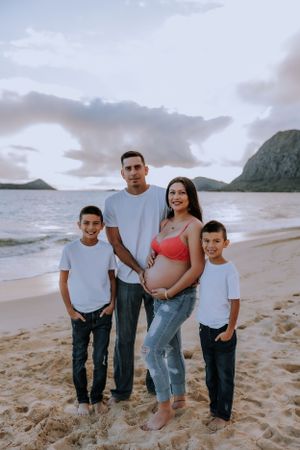 Family of four posing together on sandy beach with mountains in background.