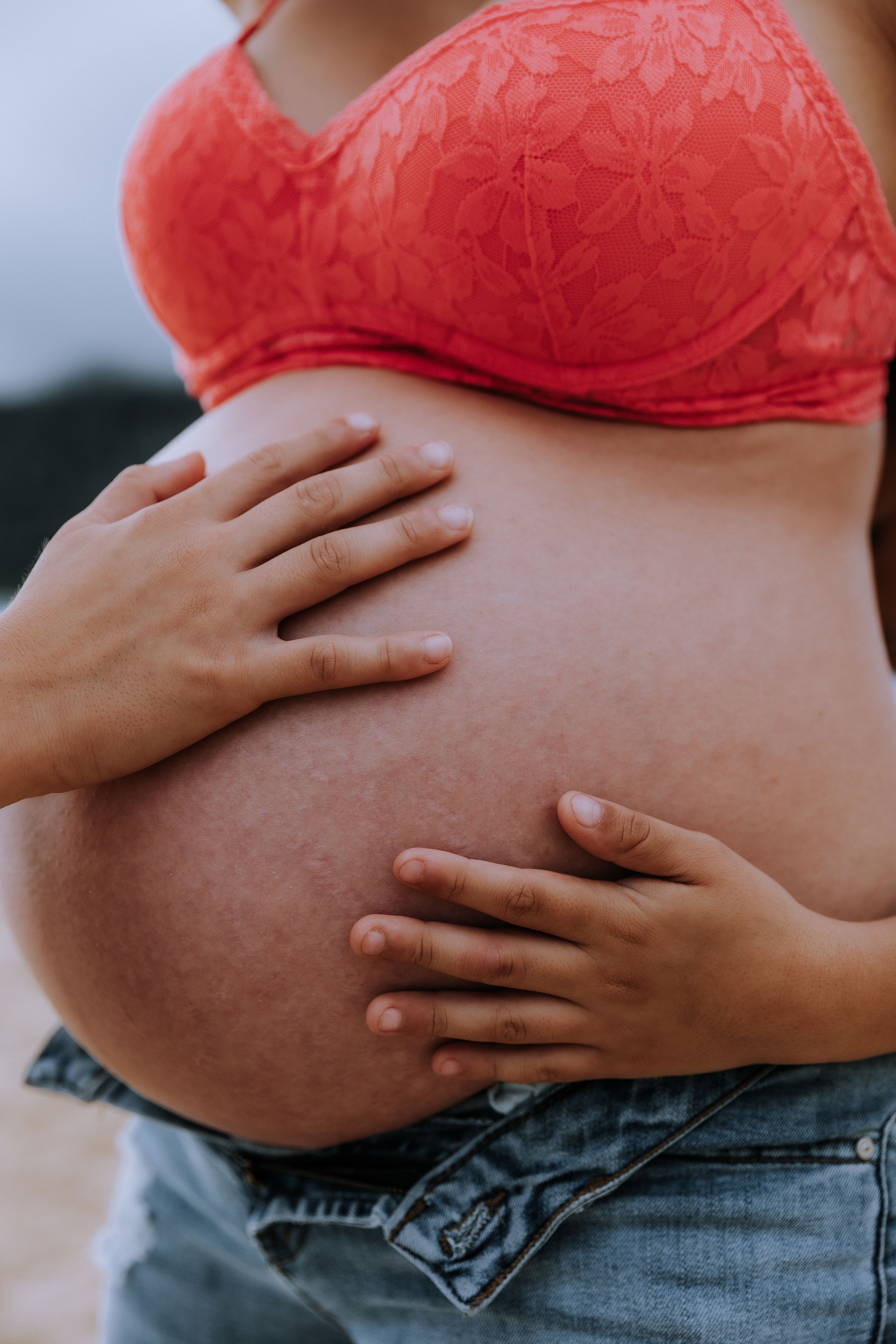 Close-up shots of a pregnant belly in a red lace bralette against beach scenery.