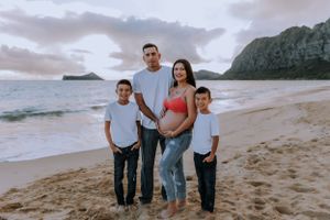 Family portrait session on a scenic Hawaiian beach with mountains in the background.