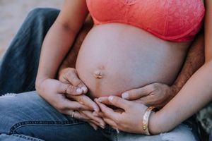 Detailed maternity photography focusing on hands cradling a pregnant belly at the beach.