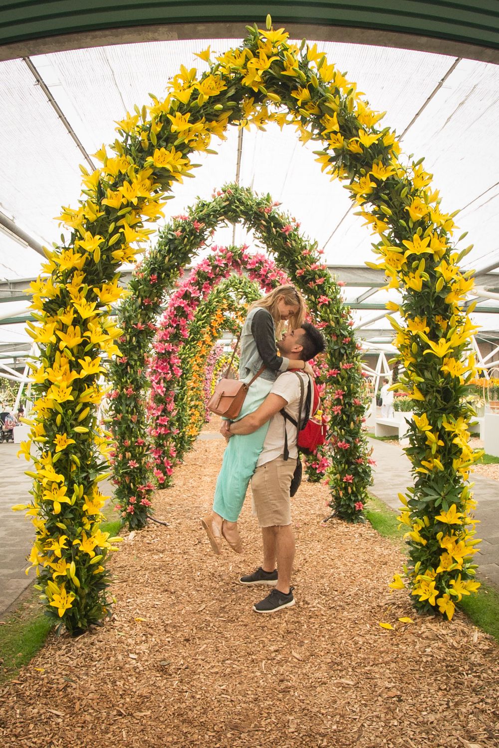 Colorful floral archway display with yellow and pink flowers in a garden setting.