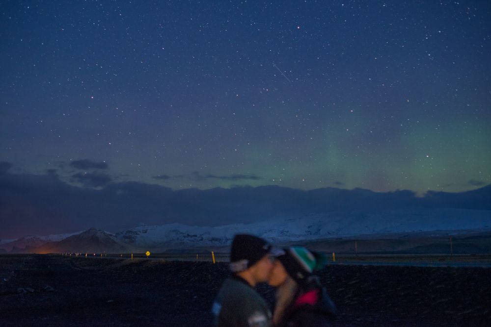 Stunning nighttime panorama showing northern lights and stars over dark landscape.