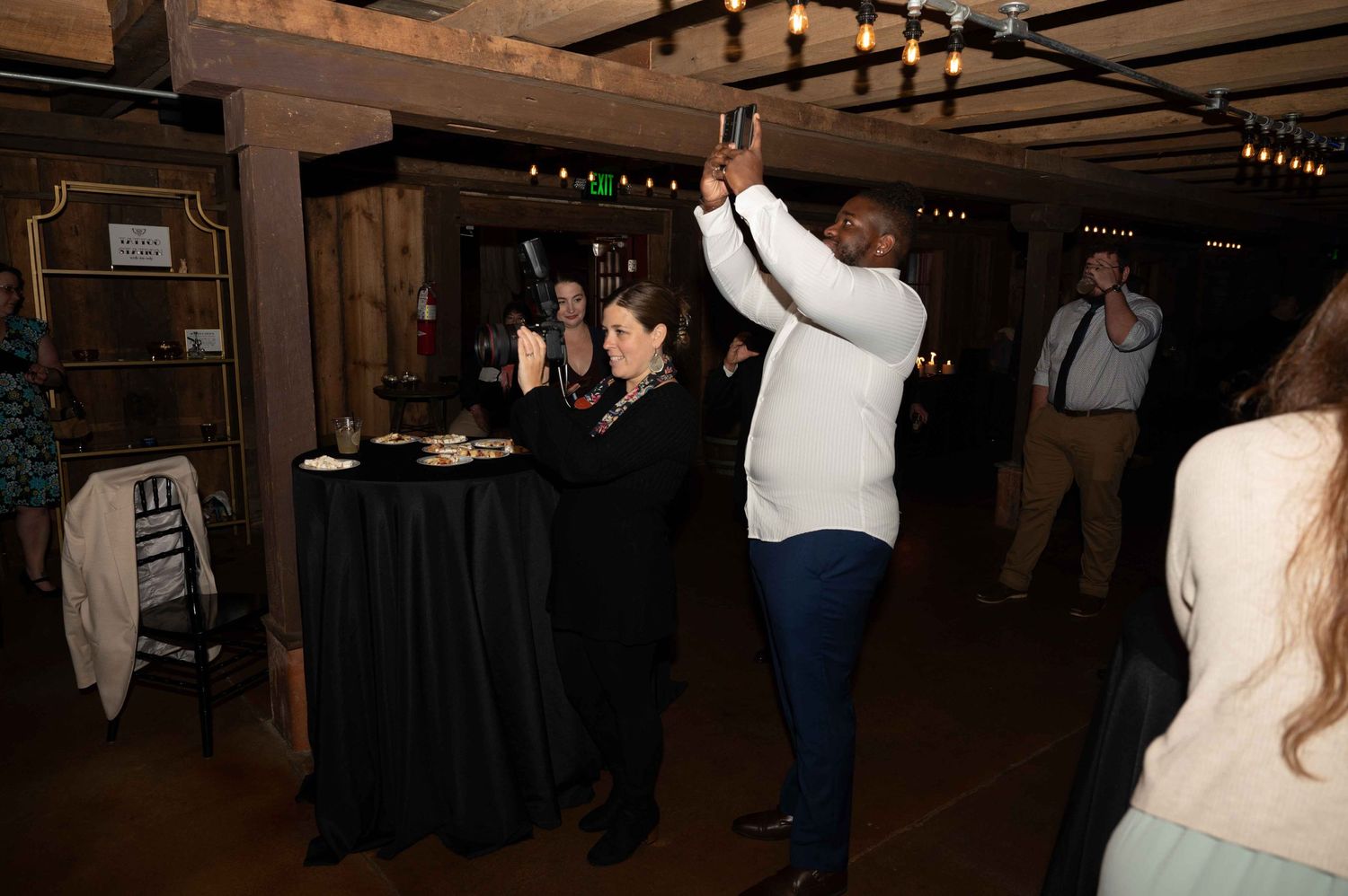 Wedding guests dancing and celebrating at a reception in a dimly lit rustic venue.