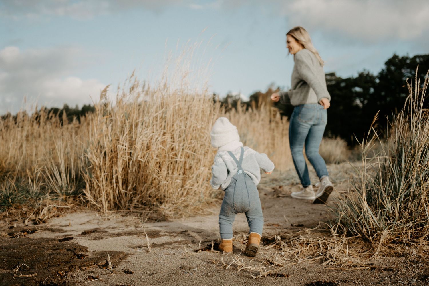 A child and adult explore together through tall autumn grass at sunset.