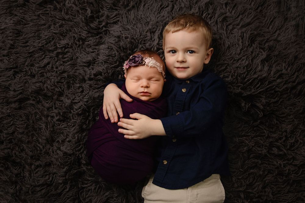 Two young children pose together on dark fur backdrop with navy and purple outfits.