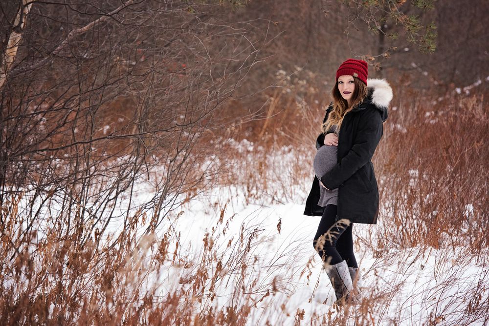 A figure in winter attire with a red hat stands in a snowy landscape among bare branches.