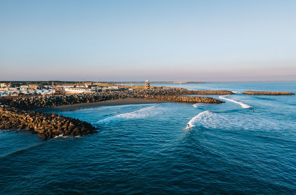 Coastal landscape with rocky breakwater and curling waves under soft morning light.