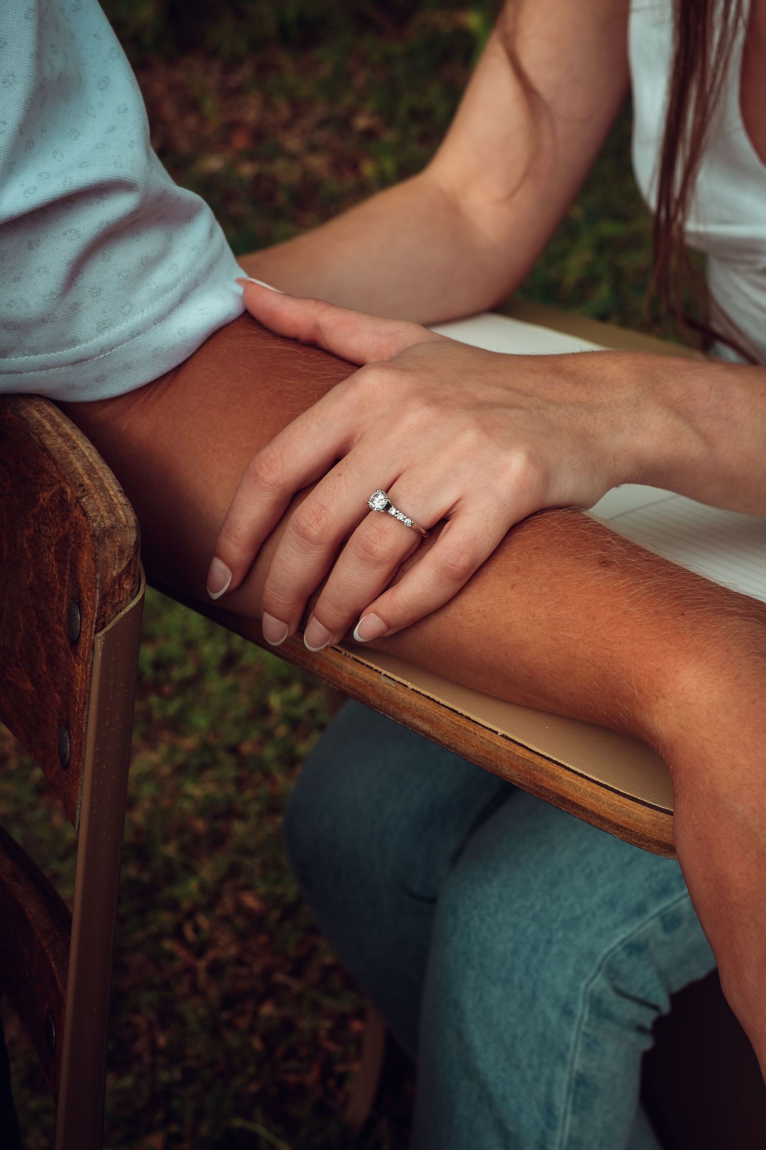 Close-up shot of hands with engagement ring resting on wooden furniture outdoors.