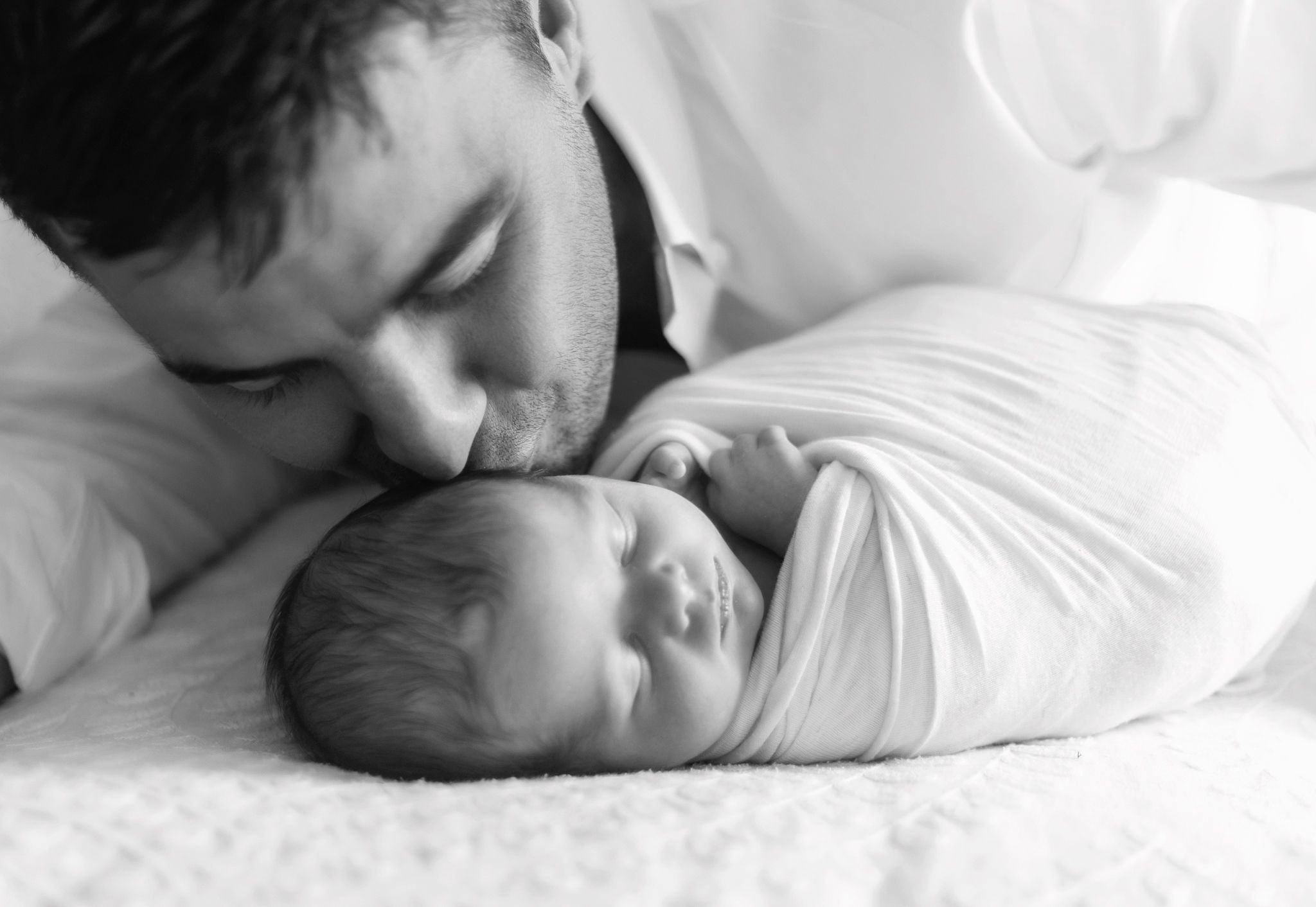A tender black and white portrait of a parent with their newborn baby.