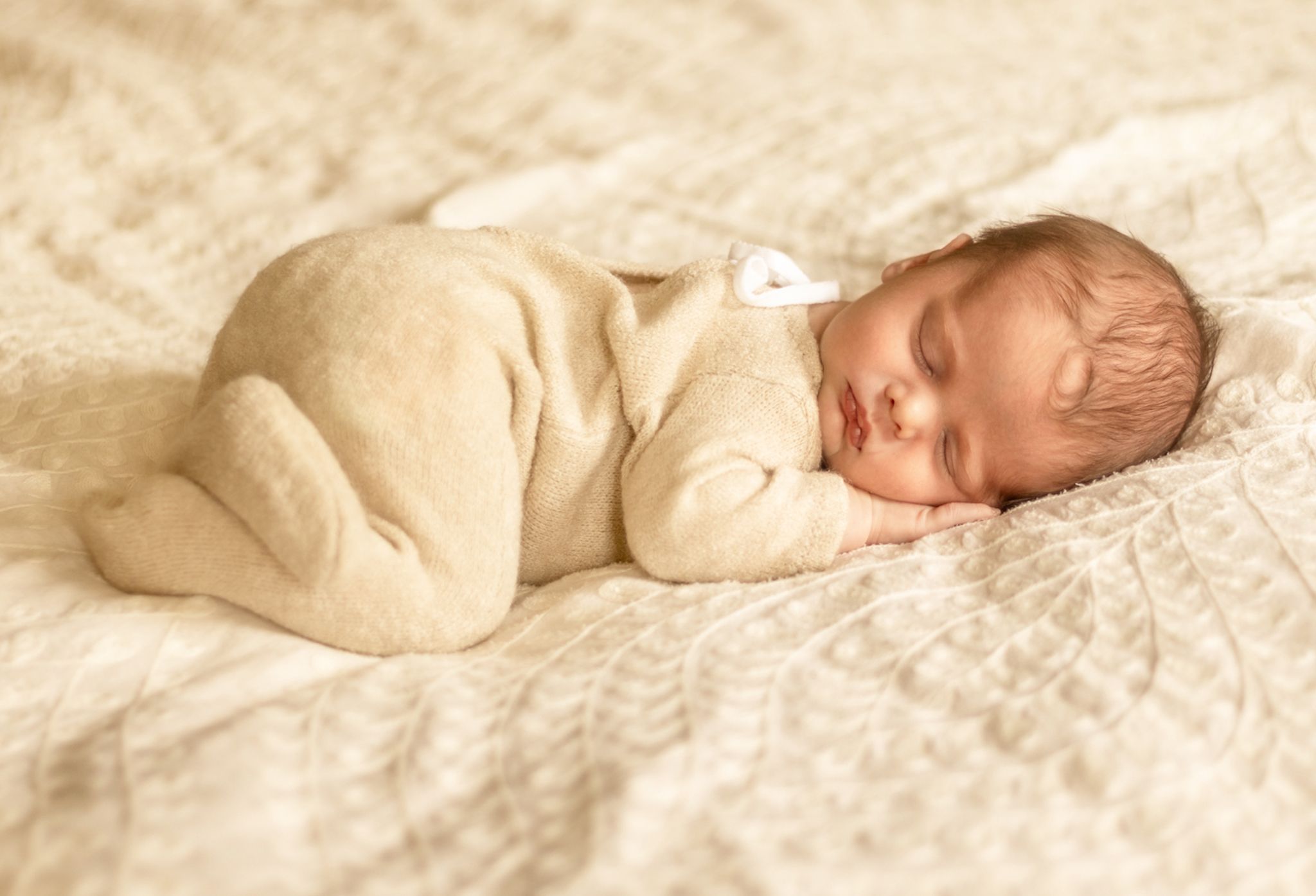 A peaceful sleeping newborn in cream colored wrapping on textured bedding.