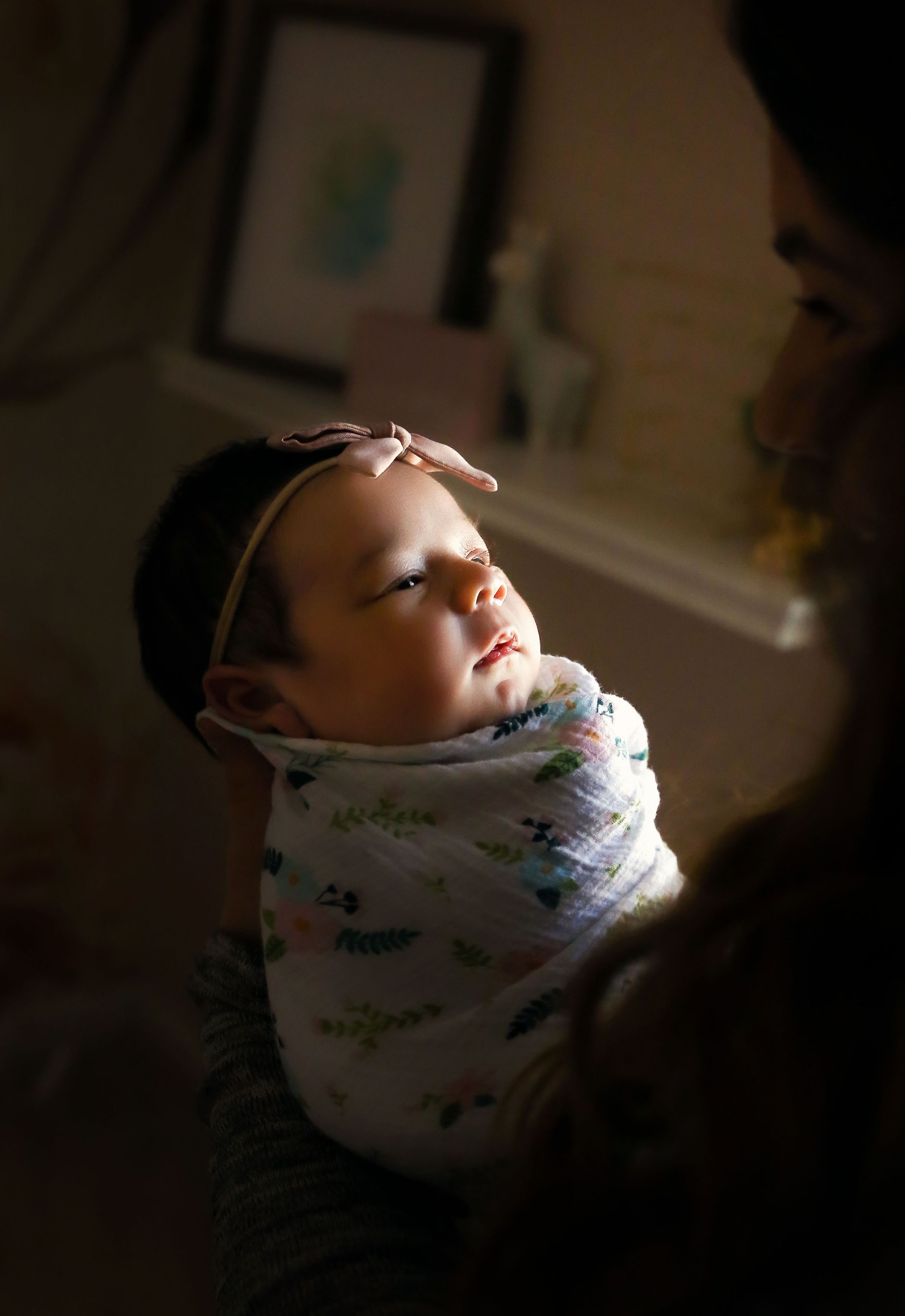 A sleeping newborn wrapped in a patterned swaddle blanket in soft indoor lighting.