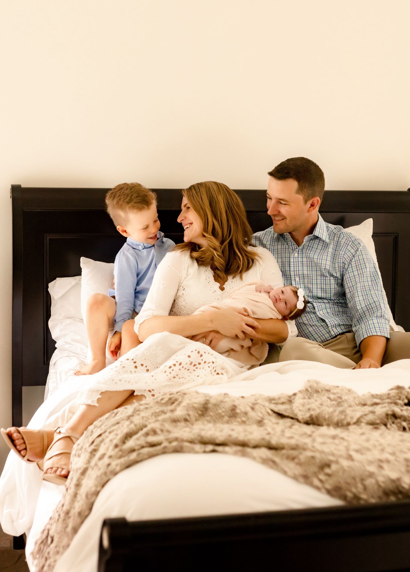 Family relaxing together on bed with newborn baby in cozy bedroom setting.