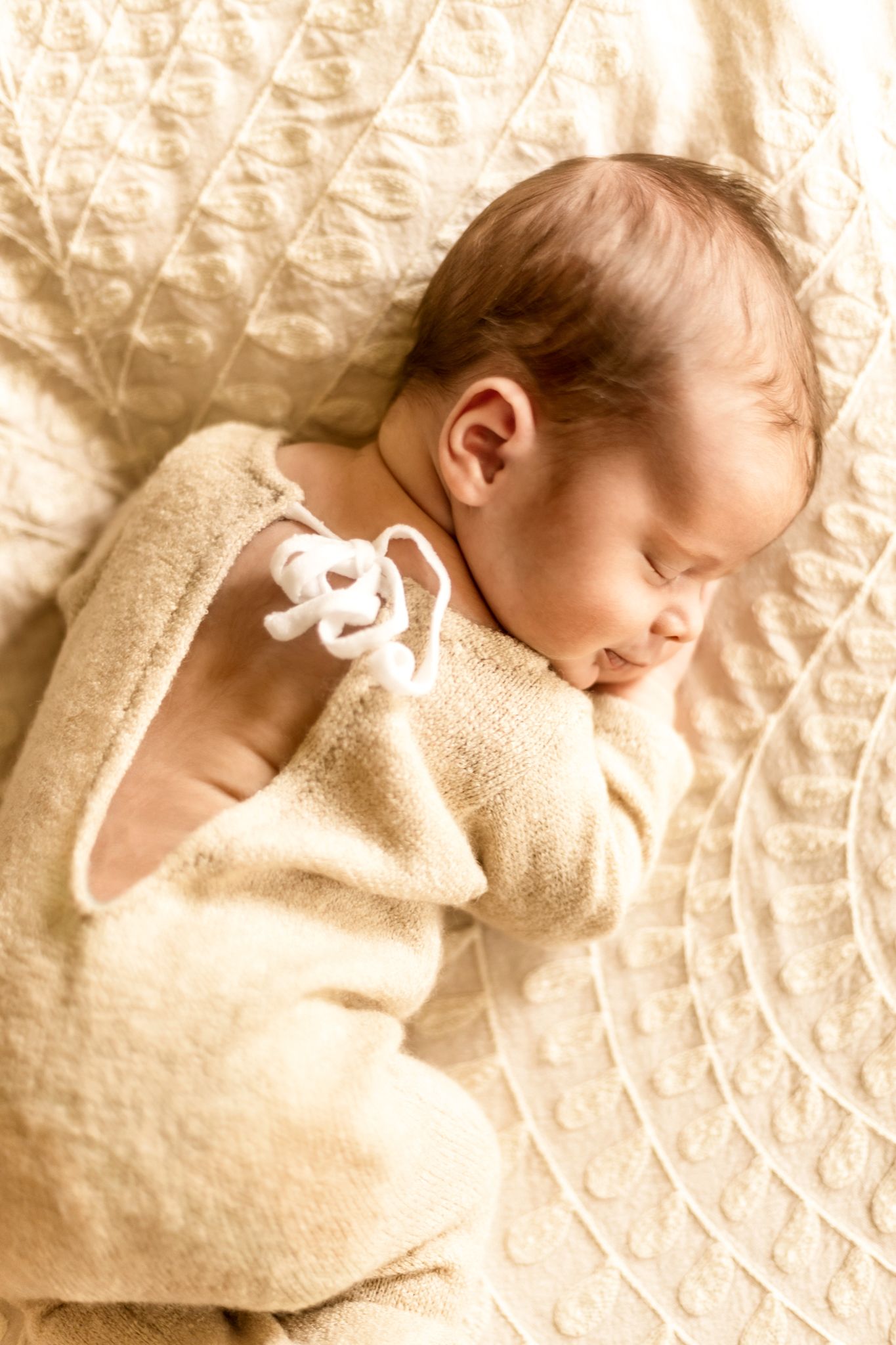 A sleeping infant wrapped in soft beige clothing on quilted fabric.