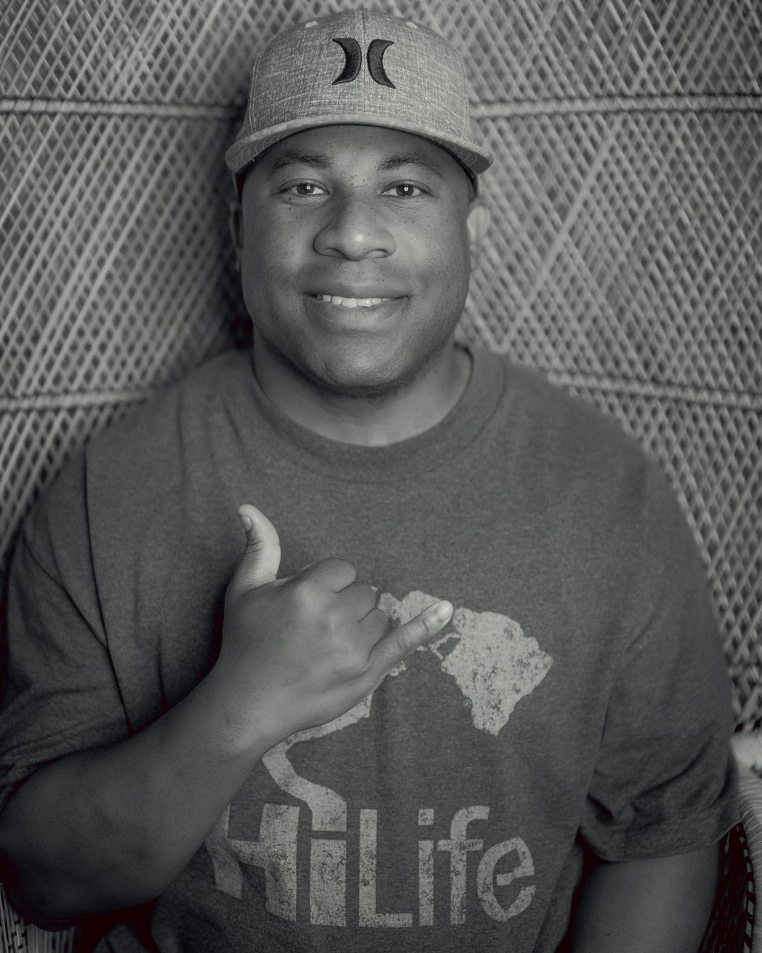 A person wearing a baseball cap with a Hurley logo gives a thumbs up while wearing a t-shirt with 'Hi Life' text.