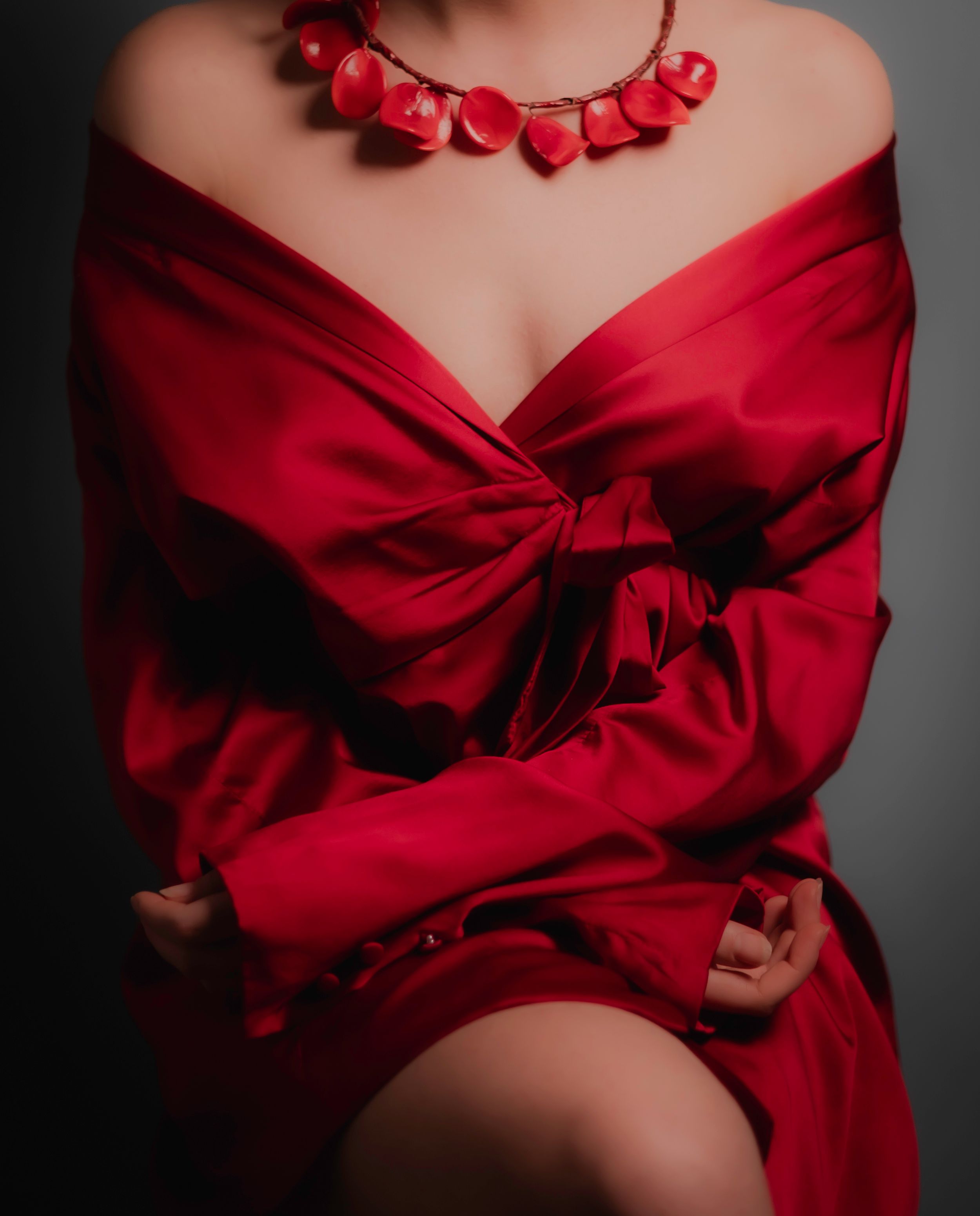Dramatic fashion portrait featuring a red silk wrap dress and matching statement necklace against dark background.