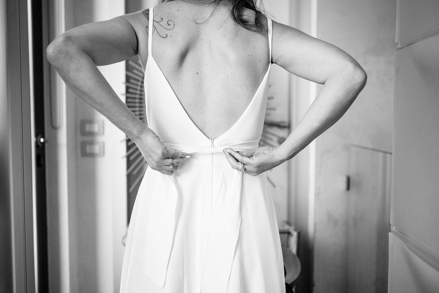 A bride ties a bow at the back of her dress while getting ready for her Italy destination wedding.