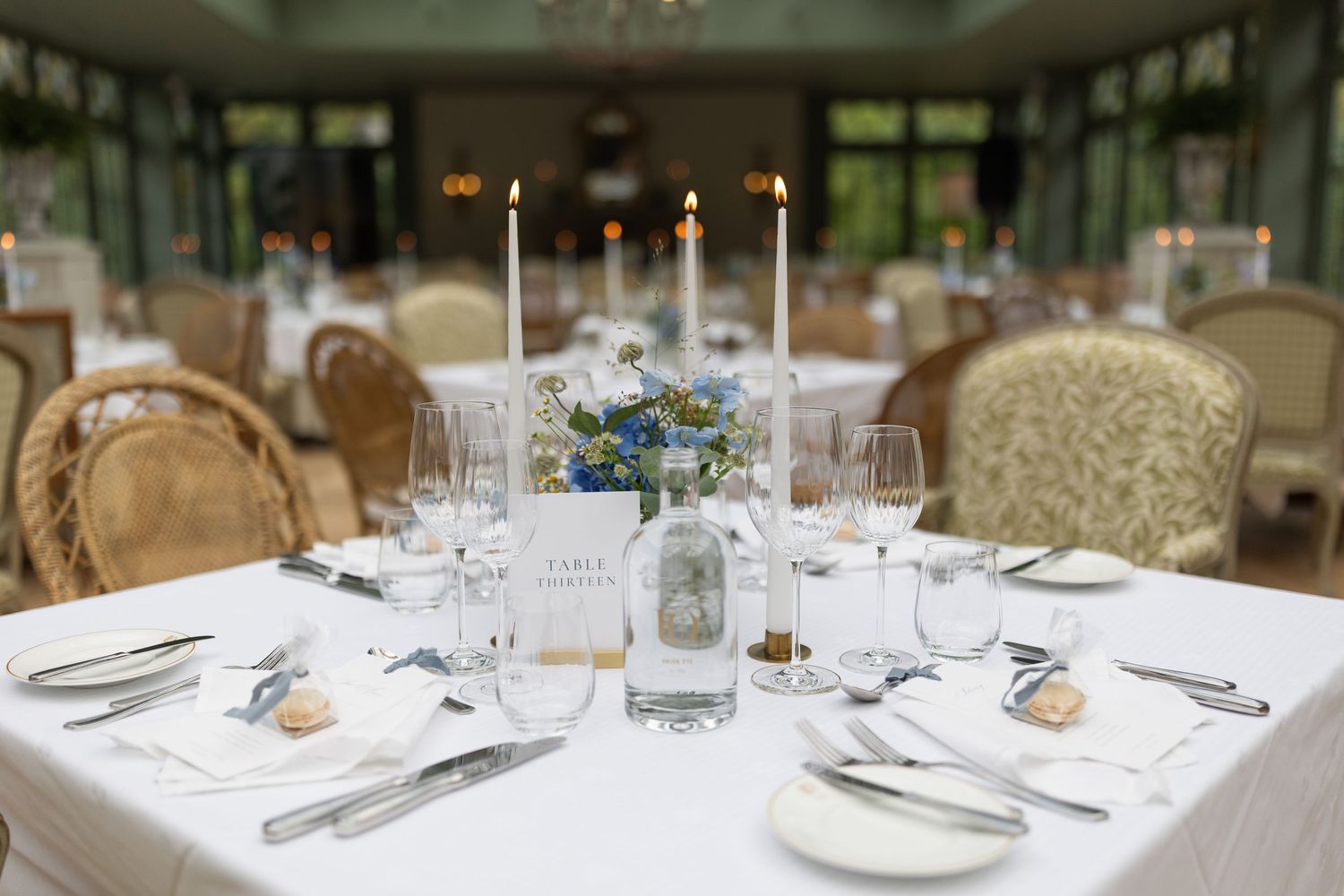 An elegant wedding table setting with white linens, candles and blue floral centerpiece.