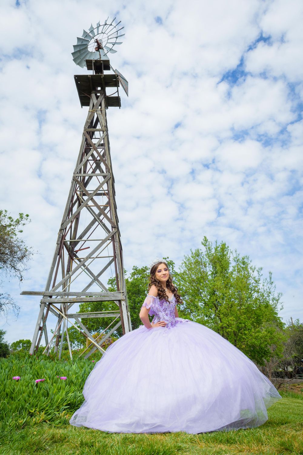 A lavender ballgown dress stands out against a rustic windmill tower and cloudy sky backdrop.
