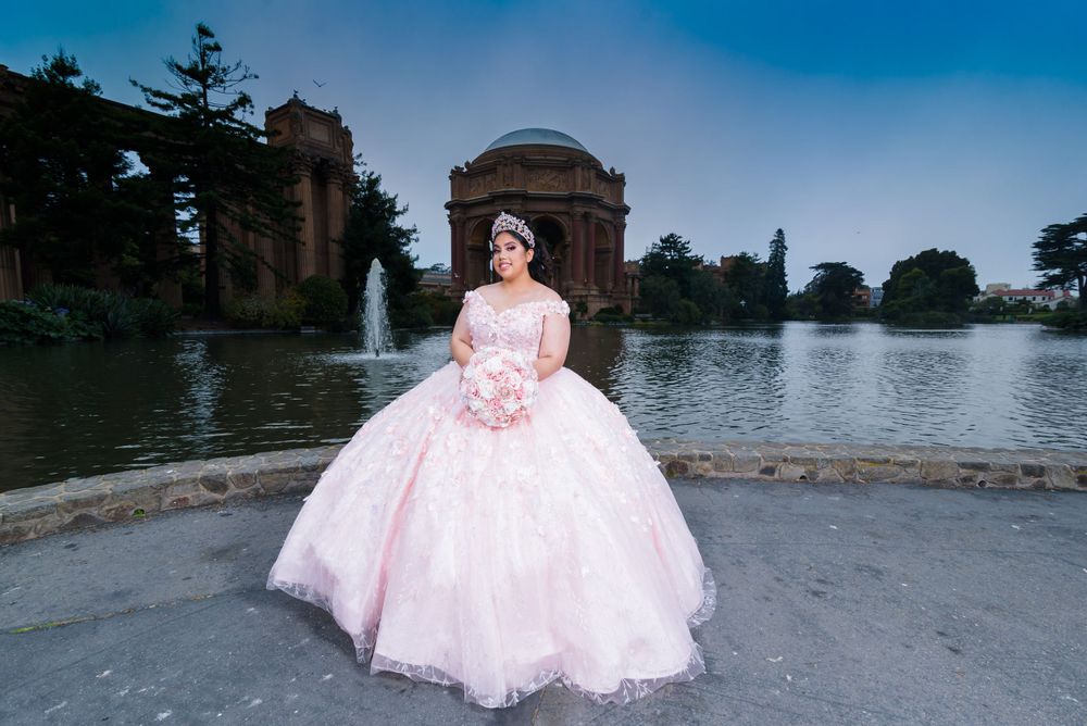 A person in a pink quinceanera dress poses at the Palace of Fine Arts in San Francisco during golden hour.