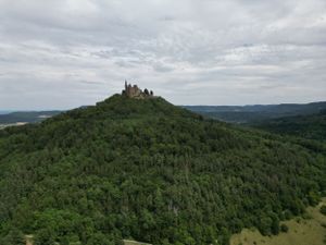 Panoramic view of a medieval castle perched atop a forested hill in Germany under cloudy skies.