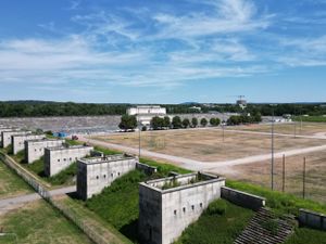 Aerial view of abandoned military bunkers and concrete structures along a grassy field under blue skies.