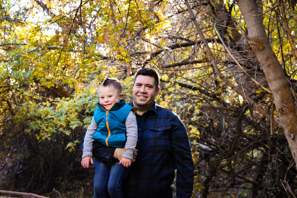 Two people share a warm moment among fall foliage and trees in an outdoor setting.
