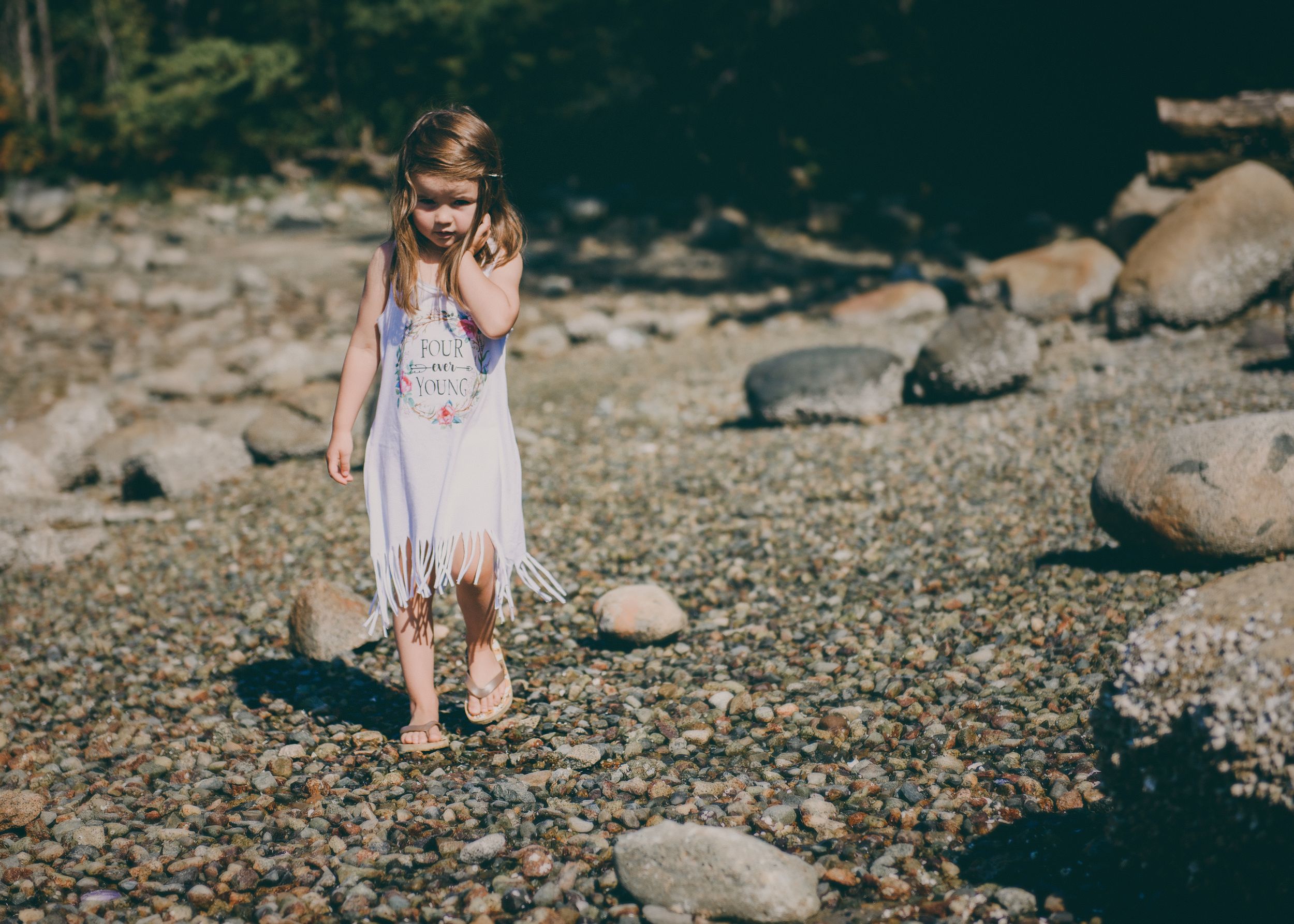 Summer scene by rocky shore with white dress and natural mountain backdrop.