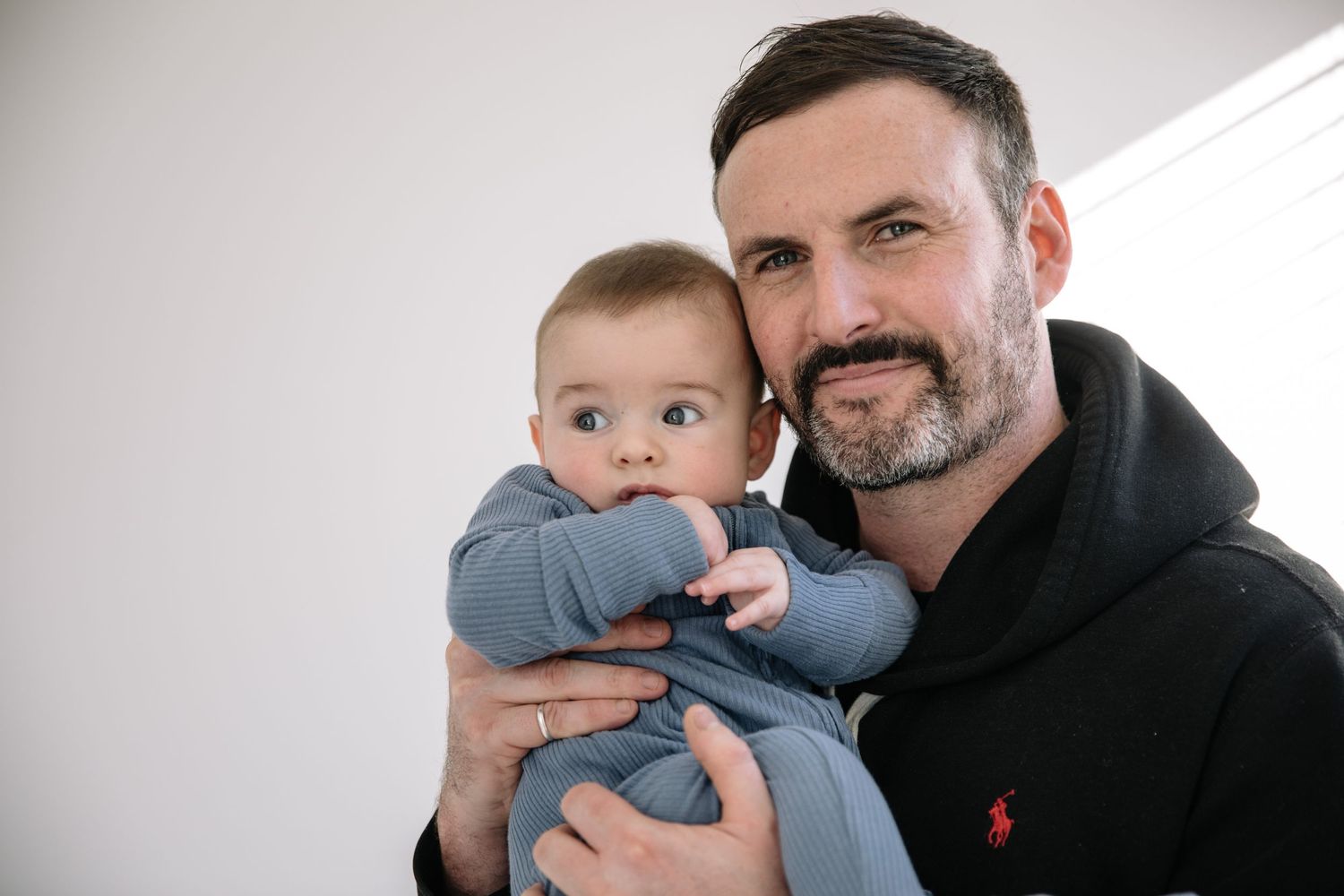 Adult holding baby wearing blue outfit against white background.