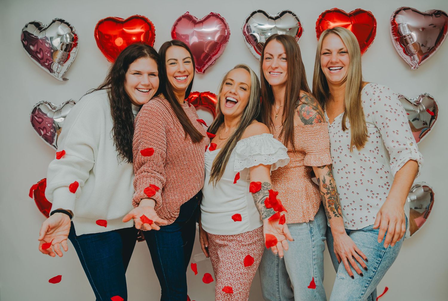 Group poses with heart balloons and confetti against white backdrop for Valentine's celebration.