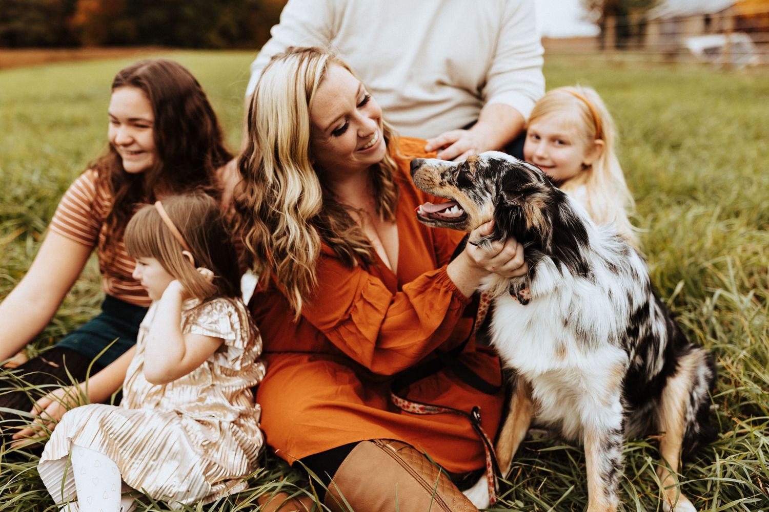 Smiling family with children and an Australian Shepherd dog sitting together in a green autumn field.