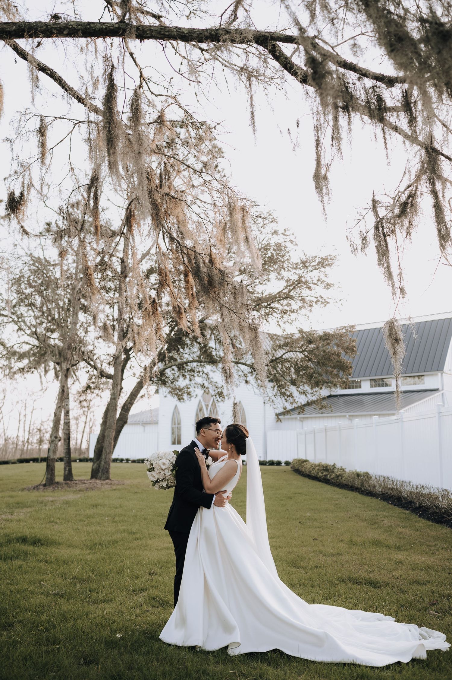 A romantic wedding portrait under Spanish moss with a white chapel in the background.