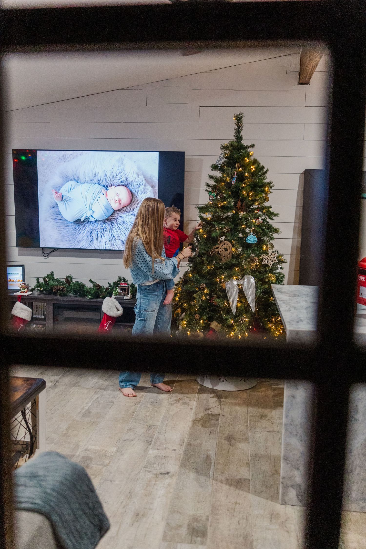 A festive living room scene with Christmas tree and TV viewed through window panes.