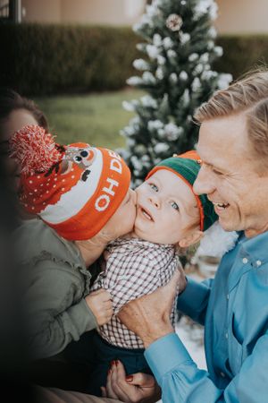 A joyful family moment captured outdoors with winter hats and a Christmas tree in the background.
